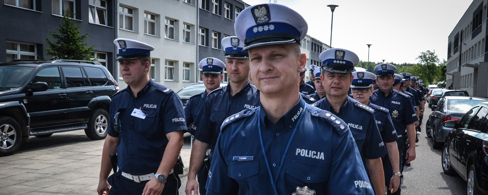Grupa poplicjantów ruchu drogowego wyrózniających sie białymi czapkami z daszkiem podczas przemarszu.