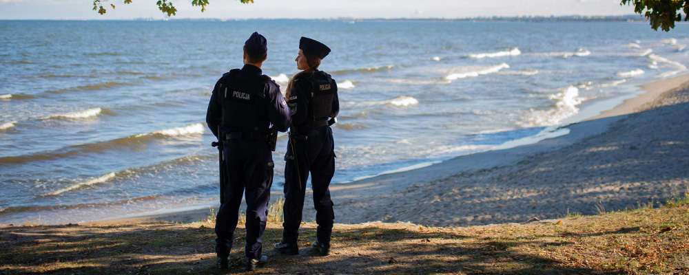 Policjant i policjantka na patrolu na plaży na tle morza.